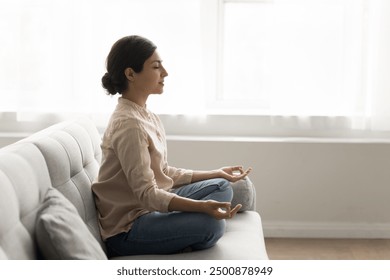 30s woman sit on sofa meditating at home, calming mind, relax body, reducing stress levels, promoting sense of inner peace, improve mental clarity, practicing mindfulness and deep breathing techniques - Powered by Shutterstock