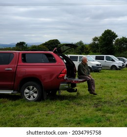 30th August 2021- A Man Sitting On The Tailgate Of His Toyota Hilux Icon D-4D 4WD DCB, Double Cab Pick-up Truck, Parked In A Public Parking Area In A Field At Beulah, Ceredigion, Wales, UK.