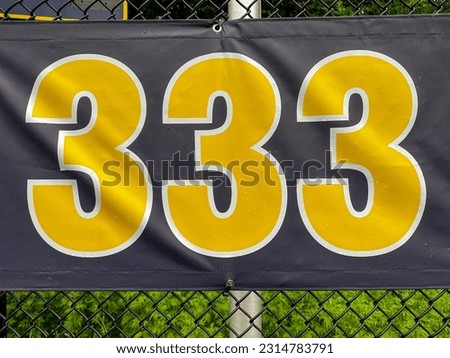 333 foot ft baseball field distance sign in yellow and black mounted on the black vinyl outfield fence.
