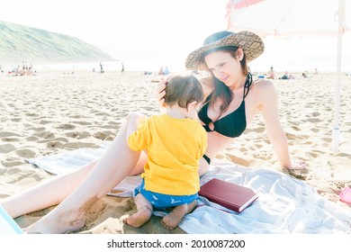 35 Year Old Millennial Woman Enjoying A Sunny Afternoon At The Beach In Summer Or Spring With Her One Year Old Son. Single Mother