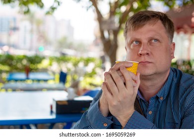 A 35-40 Year Old Man Is Lonely Sad Man Sitting With A Glass Of Coffee In A Street Cafe. A Lonely Man Sits In A Summer Cafe.