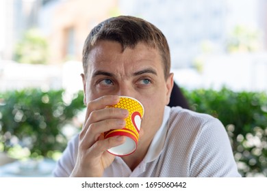 A 35-40 Year Old Man Is A Lonely Sad Man Sitting With A Glass Of Coffee In A Street Cafe