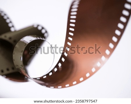 A 35mm colour roll film, curled up with shallow selective focus. Concept for analogue, vintage photography, retro photographic, high price, price rise, high costs, technology and film strip.