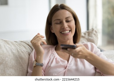 35s Attractive Woman Holds Smartphone Having Call To Friend Or Family On Speaker Phone, Using AI Browse Information Enjoy Easy Comfort Modern Tech Usage Seated On Sofa At Home, Virtual Assistant User