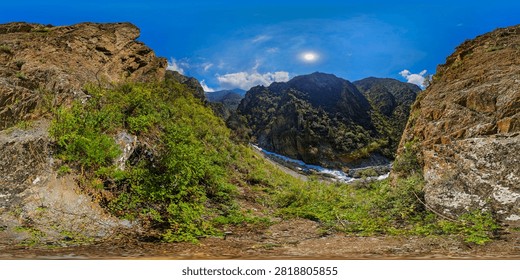 360-degree equirectangular panorama of a rugged mountain gorge in Kyrgyzstan. Steep cliffs and lush vegetation flank a turbulent river, creating a stunning natural landscape.
