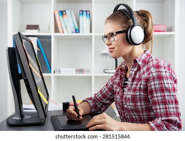 3d Animator Drawing On Graphic Tablet Listening Music In Headset. Young Positive Female Designer Holding Stylus Sitting At Computer In The Office. 