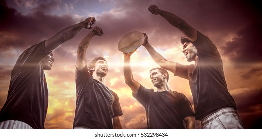 3D Blue and orange sky with clouds against rugby players cheering together with ball