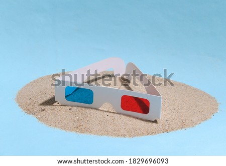 3D glasses on a sandy island. Blue studio background.