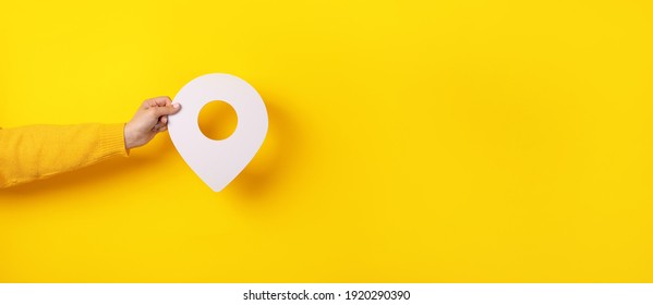 3D location symbol in hand over yellow background, panoramic image