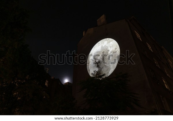 3d mapping of the moon on the wall of a building\
under a full moon at night.