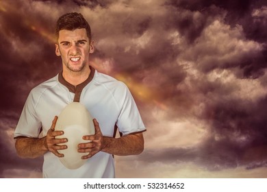 3D Portrait Of An Angry Rugby Player Holding Ball Against Gloomy Sky