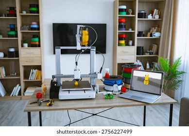 A 3D printer is actively creating a yellow object on a desk with spools of filament, tools, and a laptop displaying a 3D model