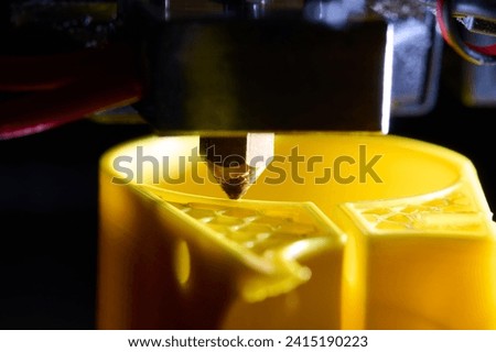 3D printer printing a part made of yellow plastic, close-up view