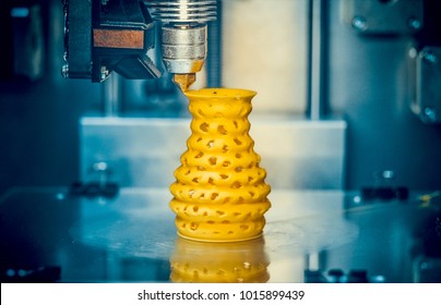3D printer prints from the plastic figure closeup. 3D printer makes yellow model close-up on gray flat surface