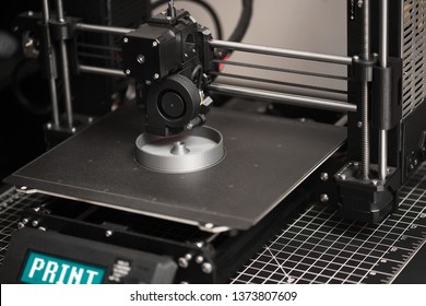 A 3D Printer In The Process Of Printing A Digital File Or Part With Gray Colored Filament On The Metal Heatbed.