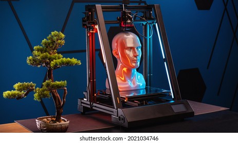 3d Printer At Work On A Bonsai Tree Table. 3d Printer Prints Head, Advertising Photo Blue And Orange Light. High Quality Photo