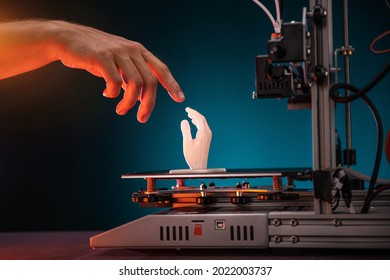 Impresión 3D en curso. La impresora 3d imprimió una mano. Un hombre toca el producto impreso en una impresora 3d. El toque de Dios, motivos bíblicos. Foto de alta calidad