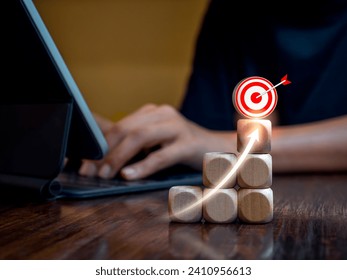 3d Target icons and rise arrow on wooden cube blocks as graph steps while businessperson working with tablet computer. Work hard to create income. Business market growth, goal and success concepts.