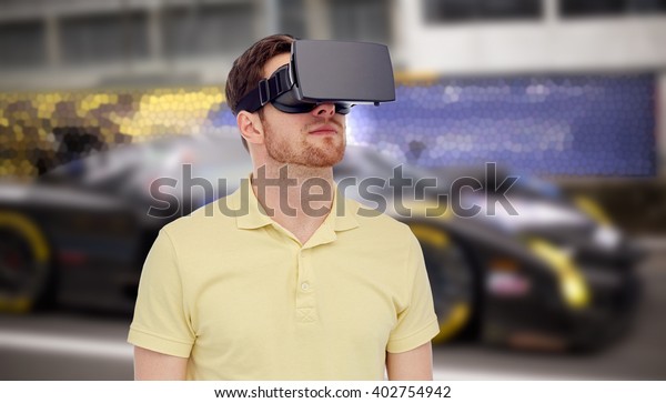 3d technology,\
virtual reality, entertainment and people concept - young man with\
virtual reality headset or 3d glasses playing car racing game over\
street race background
