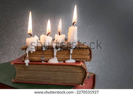 4 burning candles with dripping wax on vintage hard cover books, soft focus close up