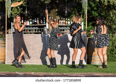 4 Girls Dance, Laugh And Drink At A Private Party In An Open-air Pub In Front Of A Bar In The Garden, Outside. They Are Dressed In Party Clothes And Black, With Sunglasses, They Are Caucasian.