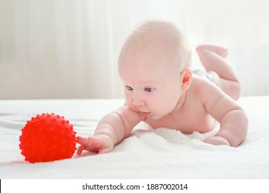 Ein viermonatiger Junge liegt auf dem Bauch, mit Betonung auf den Händen. Er versucht, nach dem roten Gummiball zu greifen. Entwicklung des Kindes.