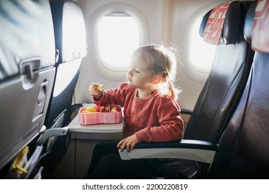 4 Year Old Preschooler Girl Eating Snacks From Lunch Box While Travelling By Plane