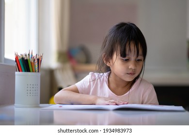 A 4 Years Old Asian Little Girl Is Reading The Book For Her Homeschooling Class , Concept Of Learning At Home Without Screen And Technology For Kid And Learn Through Play Activity For Child Education.