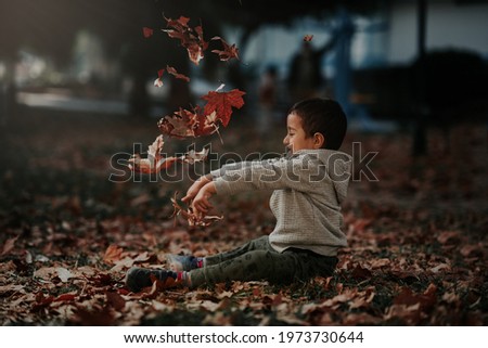 4 yearsold boy sitting and playing with dry leaf. He throws up them and looking.