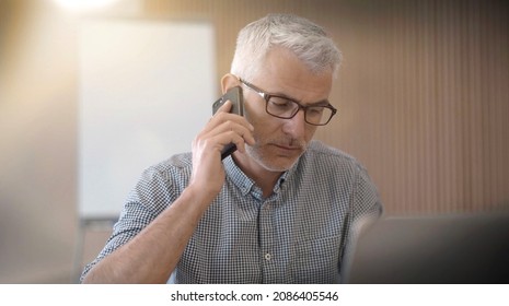 40 year old man with glasses on the phone in an office - Shutterstock ID 2086405546
