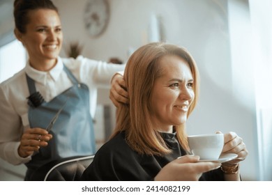 40 years old hair salon employee in modern beauty salon cutting hair with scissors and relaxed client with cup of tea. - Powered by Shutterstock