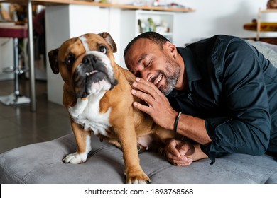 40 Years Old Man Playing With His Dog On The Couch At Home And Talking On The Phone