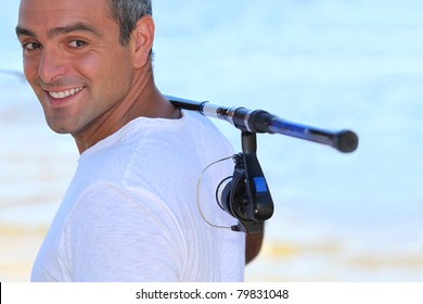 A 40 Years Old Man Walking On The Beach With A Fishing Rod On His Shoulder