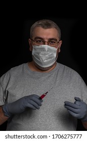 A 40-50 Year Old Man With Glasses And A Disposable Mask And Disposable Gloves Holds A Syringe With Red Liquid.