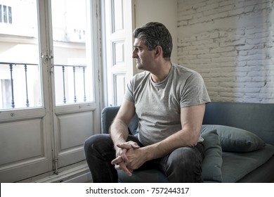 40s or 50s sad and worried man with grey hair sitting at home couch looking depressed and wasted in sadness face expression in depression and life problems concept