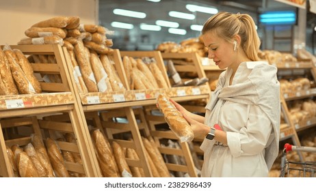 40s lady buy rye bread bakery shop. Girl take fresh baguette bakehouse. Woman smell wheat long loaf. Buyer put item store cart. Food market bakery row. Person sniff warm french breads. Sale tasty buns - Powered by Shutterstock