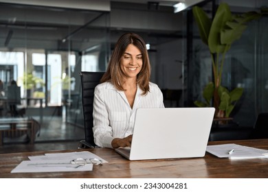 40s mid age European business woman CEO using laptop application for work sitting at table workspace in office. Smiling Latin Hispanic mature adult professional businesswoman using pc digital computer - Shutterstock ID 2343004281