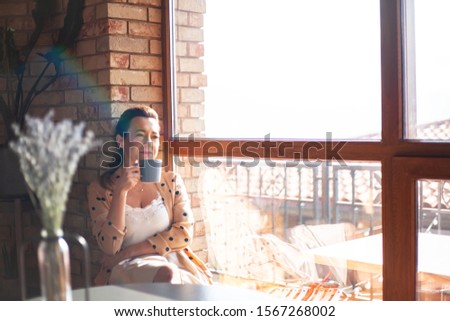 40s years woman posing in cozy cafeteria with cup of tea or coffee against the panaramic window and brick wall indoor. Female woman dressed style clothes.