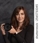 40-year-old female photographer with a playful, bold expression, holding a Nikon camera against a gray background. Her look shows professionalism, independence, and self-assurance in her craft