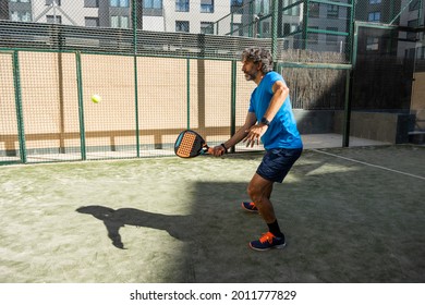 40-year-old paddle player with blue clothes, beard and grey hair, playing a game on a residential paddle court, side view. - Powered by Shutterstock