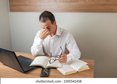 43 Year Old Man Holding His Glasses And Tired Of Reading Books.