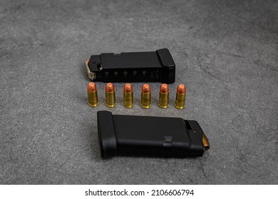 45 ACP caliber hollow point and full metal jacket bullets loaded into handgun magazines and unfired rounds lined up on a stone surface