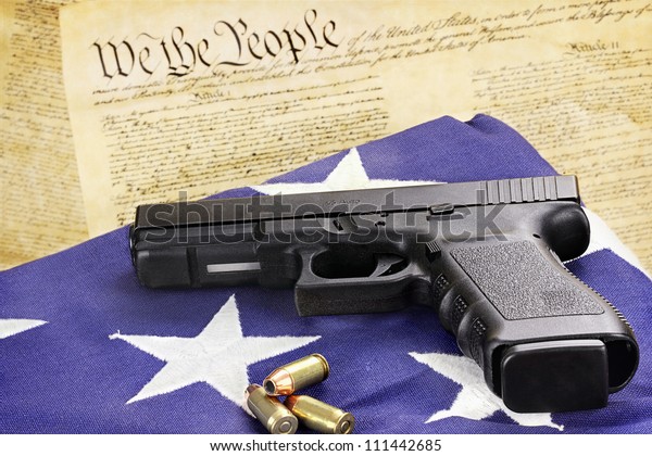 A 45 caliber handgun and\
ammunition resting on a folded flag against the United States\
constitution.