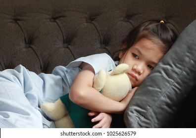 4-5 Year Old Asian Patient Kid Lie Down On Couch Or Sofa In Patient Suit With Her Doll.Skinny Kid Look Sad,tired,pain And Sick.Concept Of Childhood Cancer Awareness.