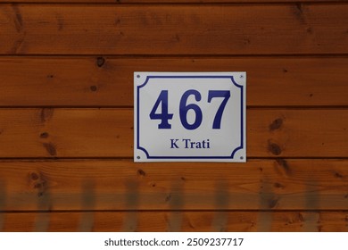 467 house number on a wooden wall background with text K trati. Number Four hundred and sixty seven. 