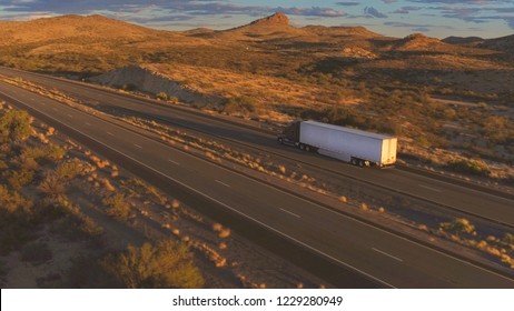 4K AERIAL: Cars and freight semi truck driving on busy highway across the country in beautiful summer evening. People on road trip traveling on busy freeway at golden sunset