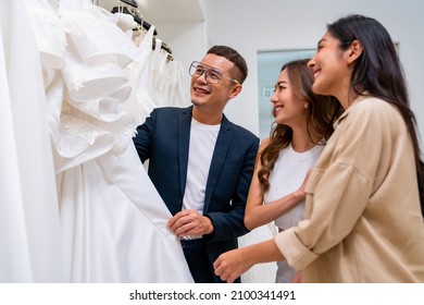 4K Asian LGBTQ Guy Bridal Shop Owner Helping Woman Lesbian Gay Couple Choosing Wedding Gown At Wedding Studio. Diversity Sexual Equality, Lgbtq Pride, Marriage Equality And Same-sex Marriage Concept.