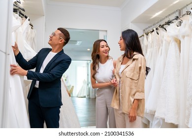 4K Asian LGBTQ Guy Bridal Shop Owner Helping Woman Lesbian Gay Couple Choosing Wedding Gown At Wedding Studio. Diversity Sexual Equality, Lgbtq Pride, Marriage Equality And Same-sex Marriage Concept.