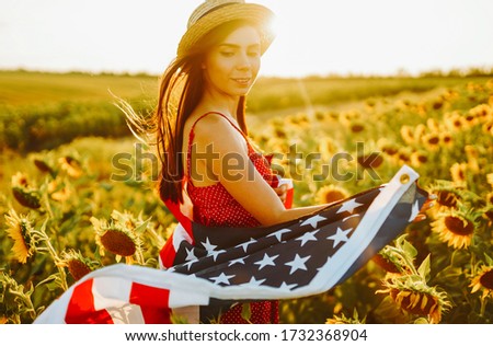 4th of July. Amazing girl in hat with the American flag in a sunflower field. Freedom day. Sunset light. Independence Day. Patriotic concept