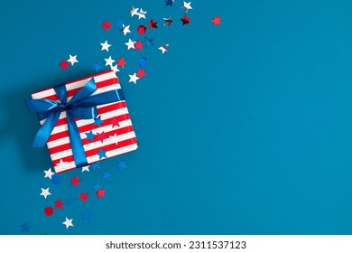 4th of July, USA Presidents Day, Independence Day, US election concept. Gift striped box with bow, star confetti on blue background. Flat lay, top view, copy space, banner - Shutterstock ID 2311537123